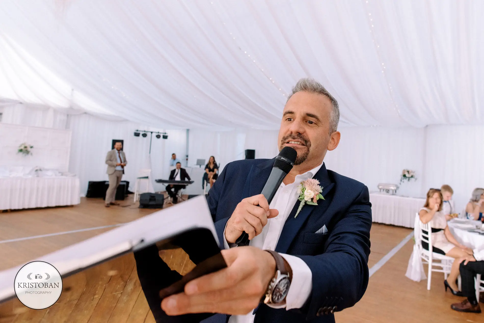 A ceremóniamester az esküvőn a mikrofon mögött, lendülettel és lelkesedéssel szólítja meg a vendégeket. Bagi Péter – ceremóniamester