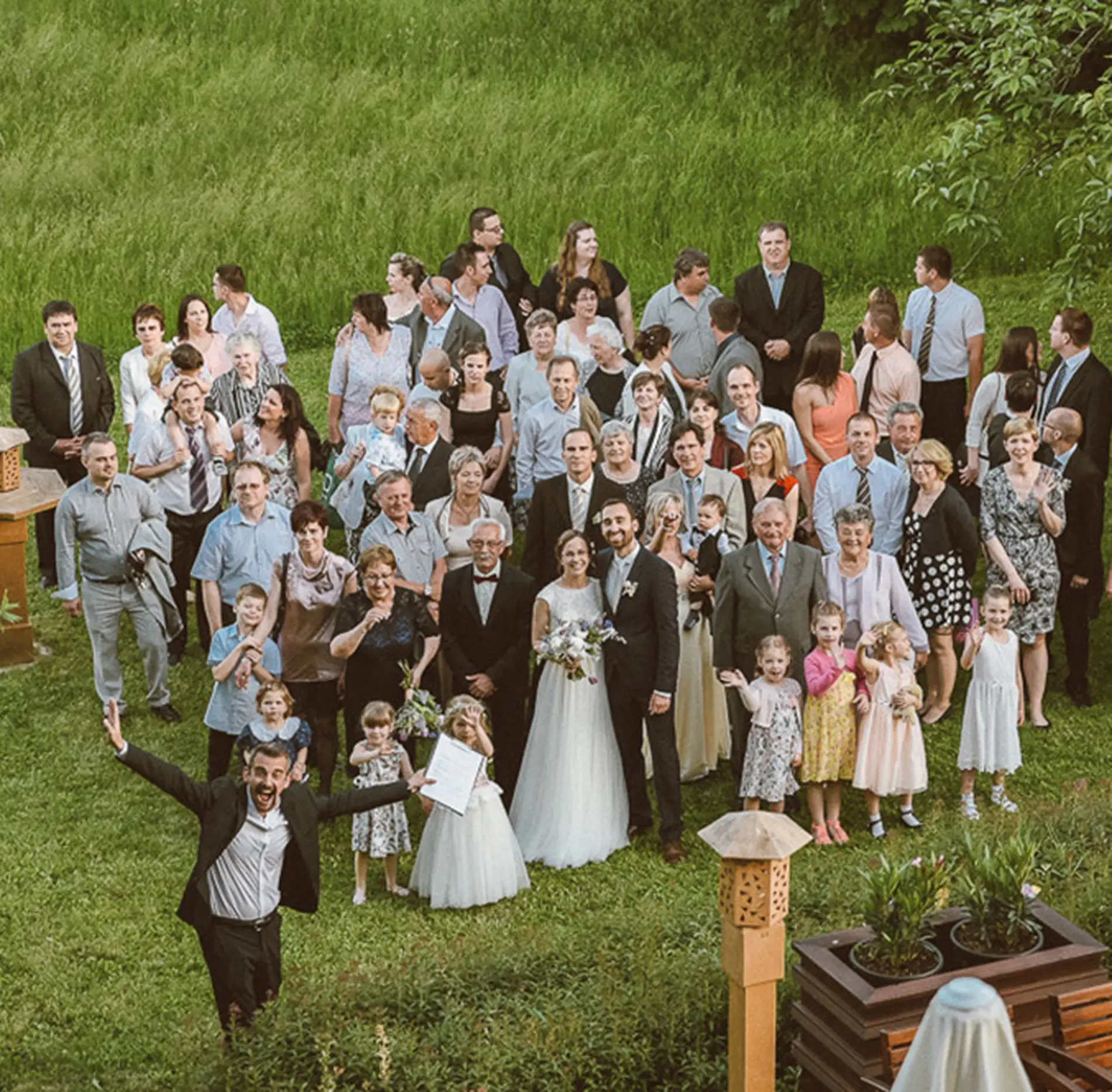 A ceremóniamester vidáman integet az esküvői csoportkép közepén, mindenki mosolyog. Bagi Péter – ceremóniamester