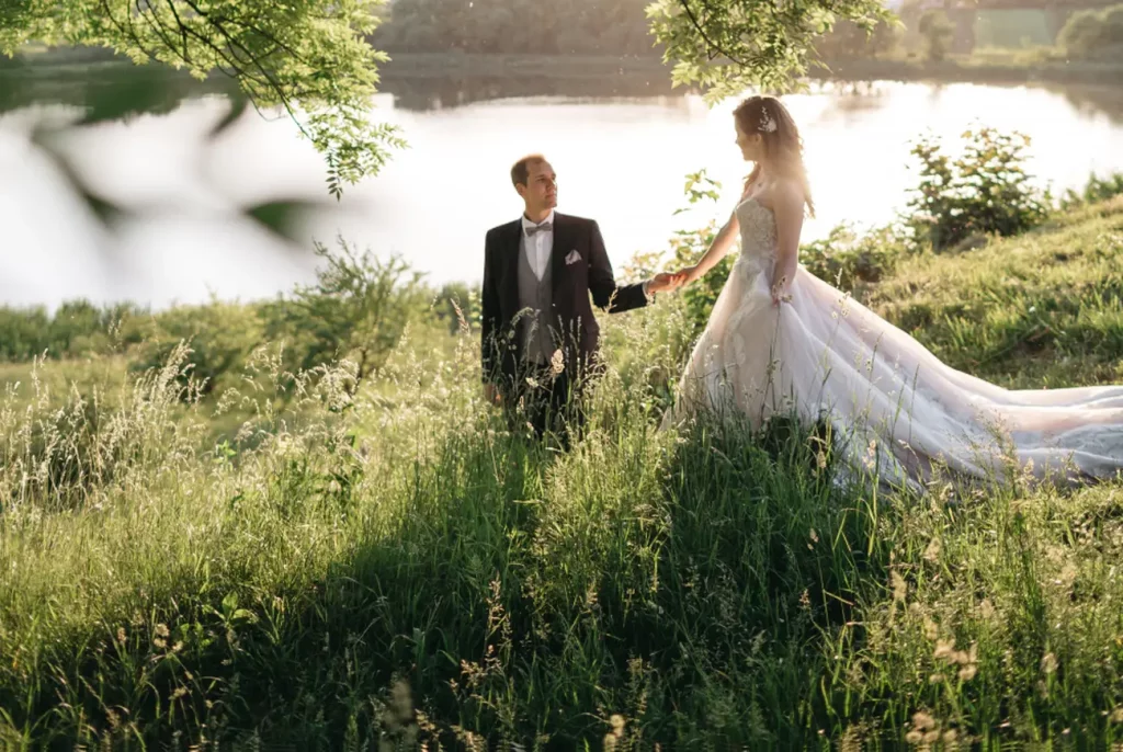 A ceremóniamester által koordinált romantikus esküvő tóparti pillanata, ahol a pár kézen fogva sétál a napfényben. Bagi Péter – ceremóniamester